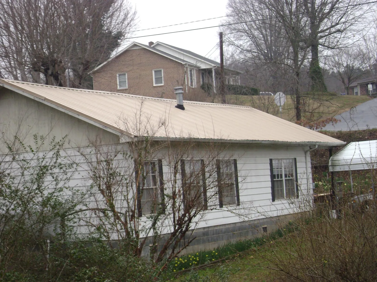 Tan metal roof on a white sided house set into a hillside — Commercial Roofing by Roofing Brothers in Sullivans Island